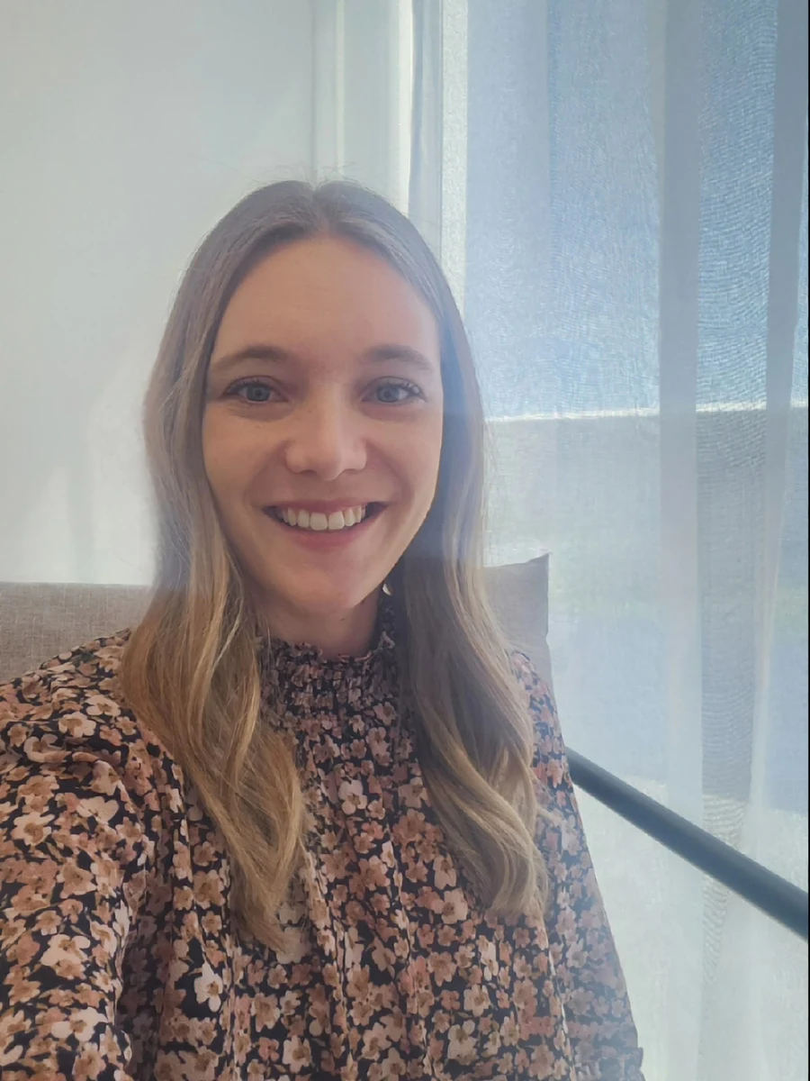 Tamsyn Berthelsen, smiling, seated by a sunlit window in her practice